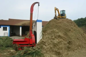 chaff cutter expelling chopped crop while an excavator piles up the material.