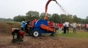 Farmers demonstrating a blue silage cutter machine outdoors while onlookers observe the chopping process.