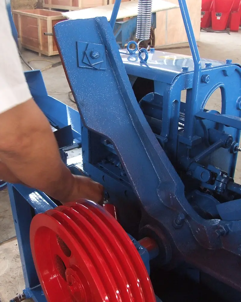 Engineer adjusting internal gears and red pulley of an industrial blue chaff cutter machine