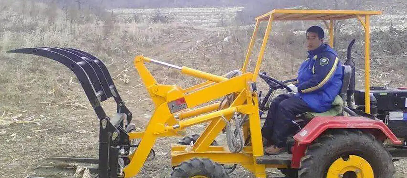 Operator working a Golden Machinery grass loader with grapple in a hillside field